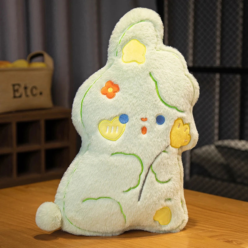 a sweet, candy shaped green bunny cushion with rosy yellow love heart cheeks, flowers in its hair, and holding a flower