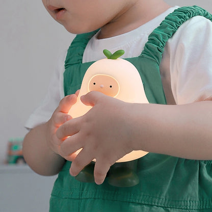 a white silicone cartoon pear night light being held by a toddler