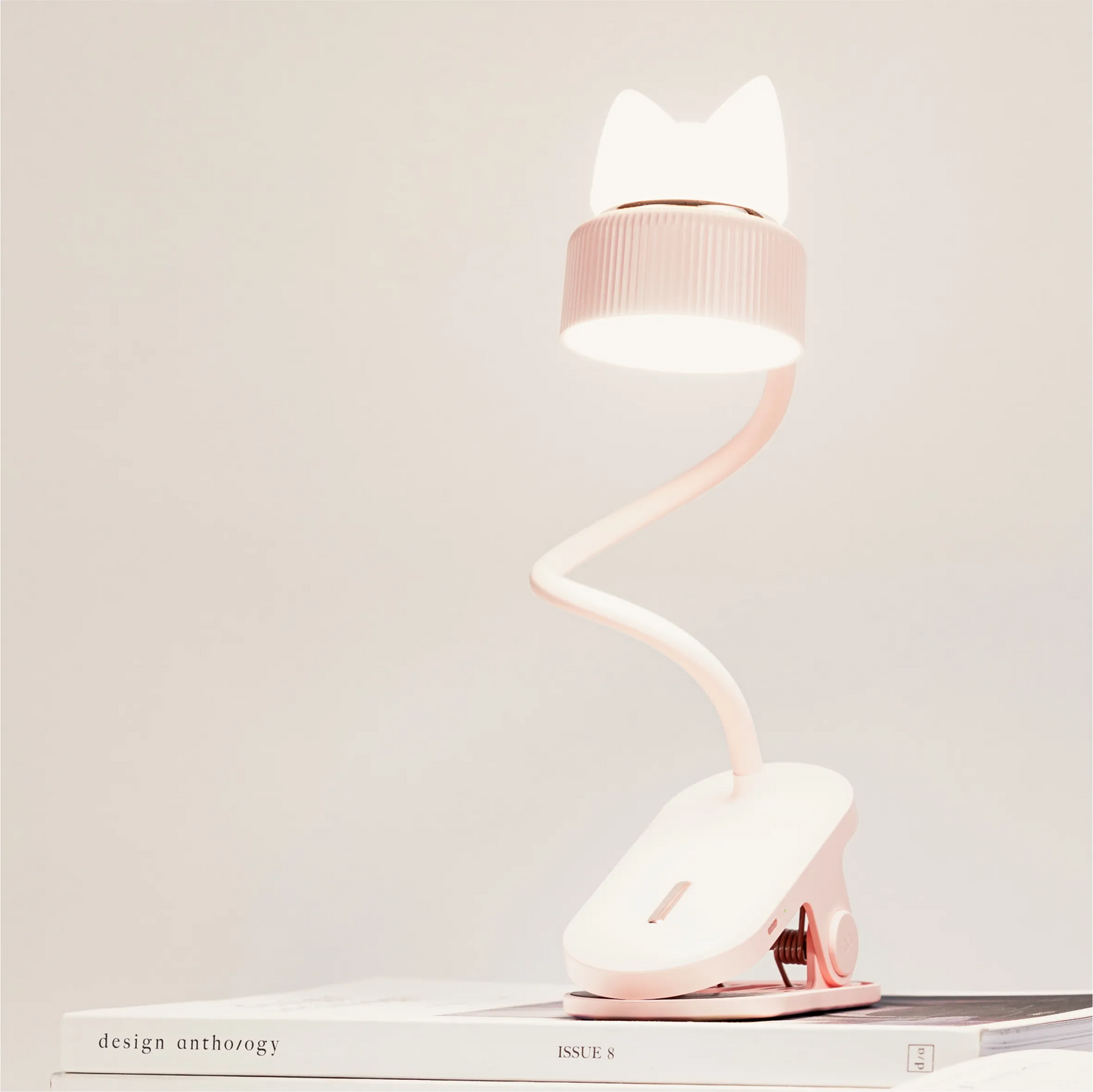 a pink desk lamp with a clip base, bendable neck and both its directional light and silicone kitten ear night light turned on