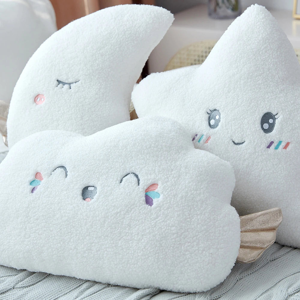 white moon, cloud, and star cushions with golden wings and pastel eyes and mouths on a bed