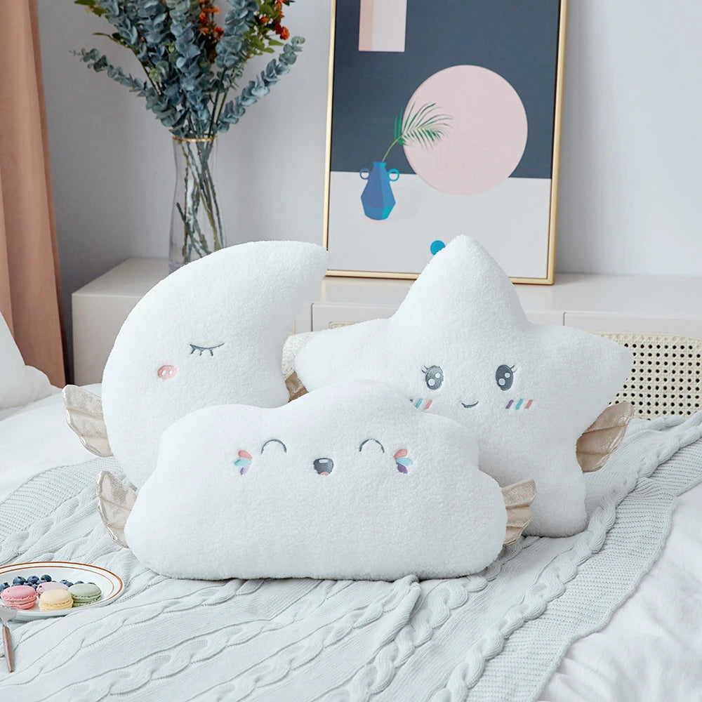 white moon, cloud, and star cushions with golden wings and pastel eyes and mouths on a bed