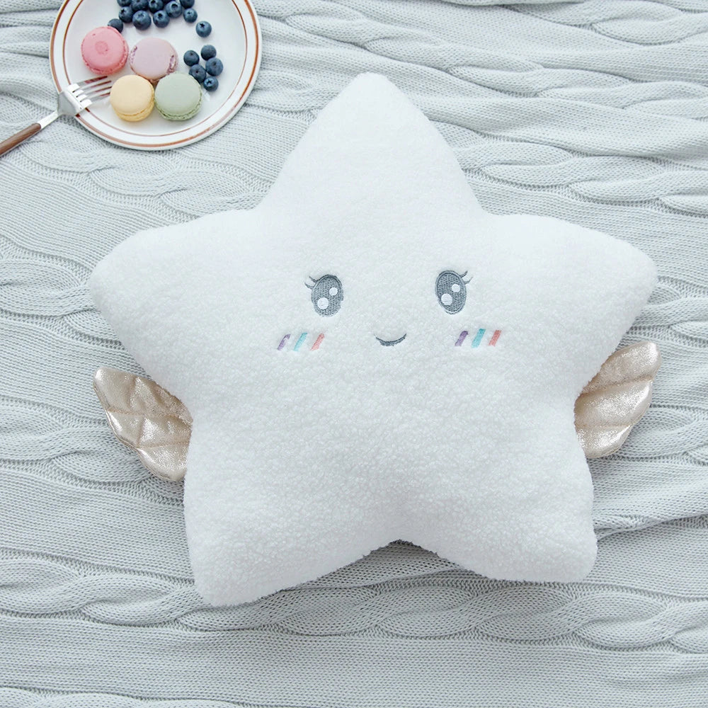 a white star cushion with golden wings and pastel eyes and mouths on a bed