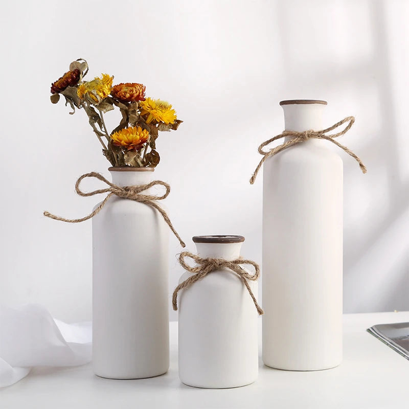 three rustic matte white ceramic flower vases shaped like bordeaux wine bottles with twine bows around their necks