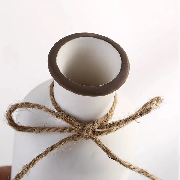 the neck of a rustic matte white ceramic flower vase shaped like a bordeaux wine bottle adorned with a twine bow