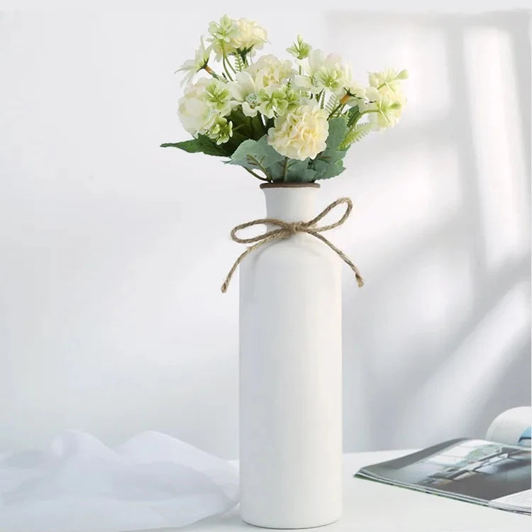 a large rustic matte white ceramic flower vase shaped like a bordeaux wine bottle with a twine bow around its neck