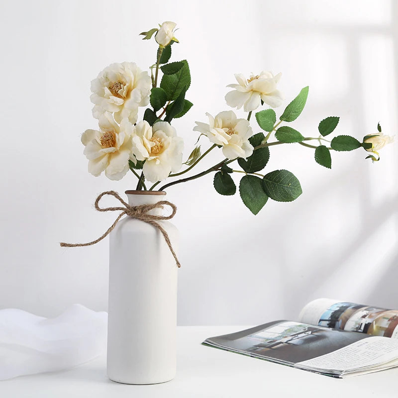 a medium rustic matte white ceramic flower vase shaped like a bordeaux wine bottle with a twine bow around its neck