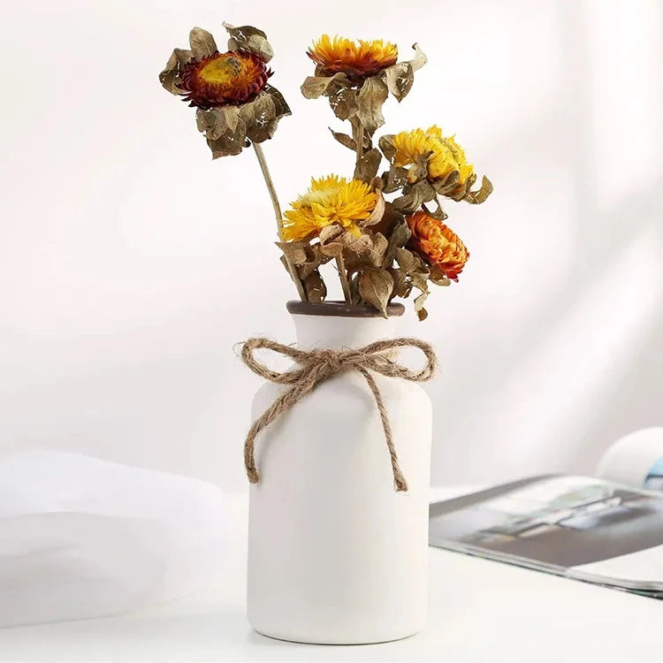 a small rustic matte white ceramic flower vase shaped like a bordeaux wine bottle with a twine bow around its neck