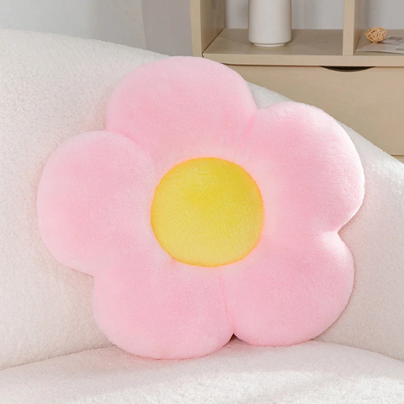 a pastel daisy cushion with pink petals and a yellow centre on a couch