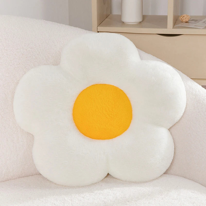 a pastel daisy cushion with white petals and a yellow centre on a couch