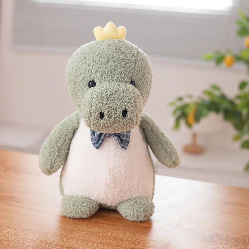 a green dinosaur soft toy wearing a dark blue bow tie and small yellow crown