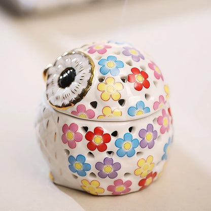 a white ceramic owl incense holder with gold highlights and a pink, yellow, purple, blue, and red flower pattern