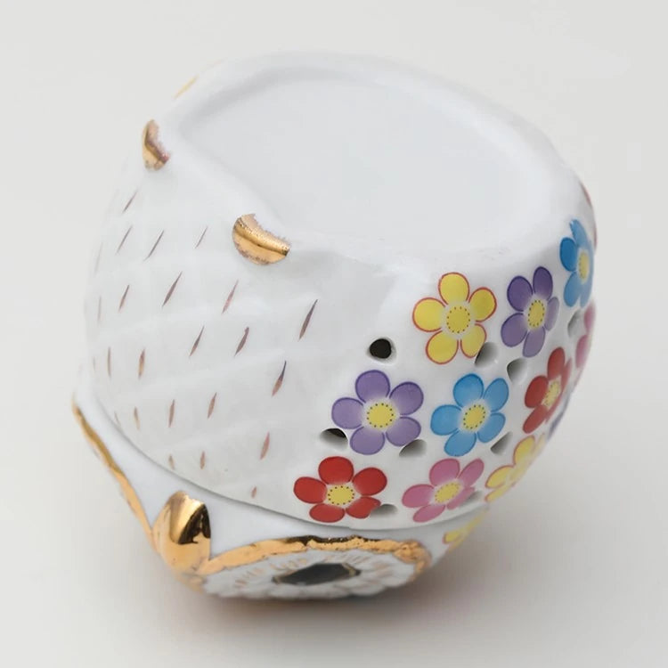 the bottom of a white ceramic owl incense holder with gold highlights and a pink, yellow, purple, blue, and red flower pattern